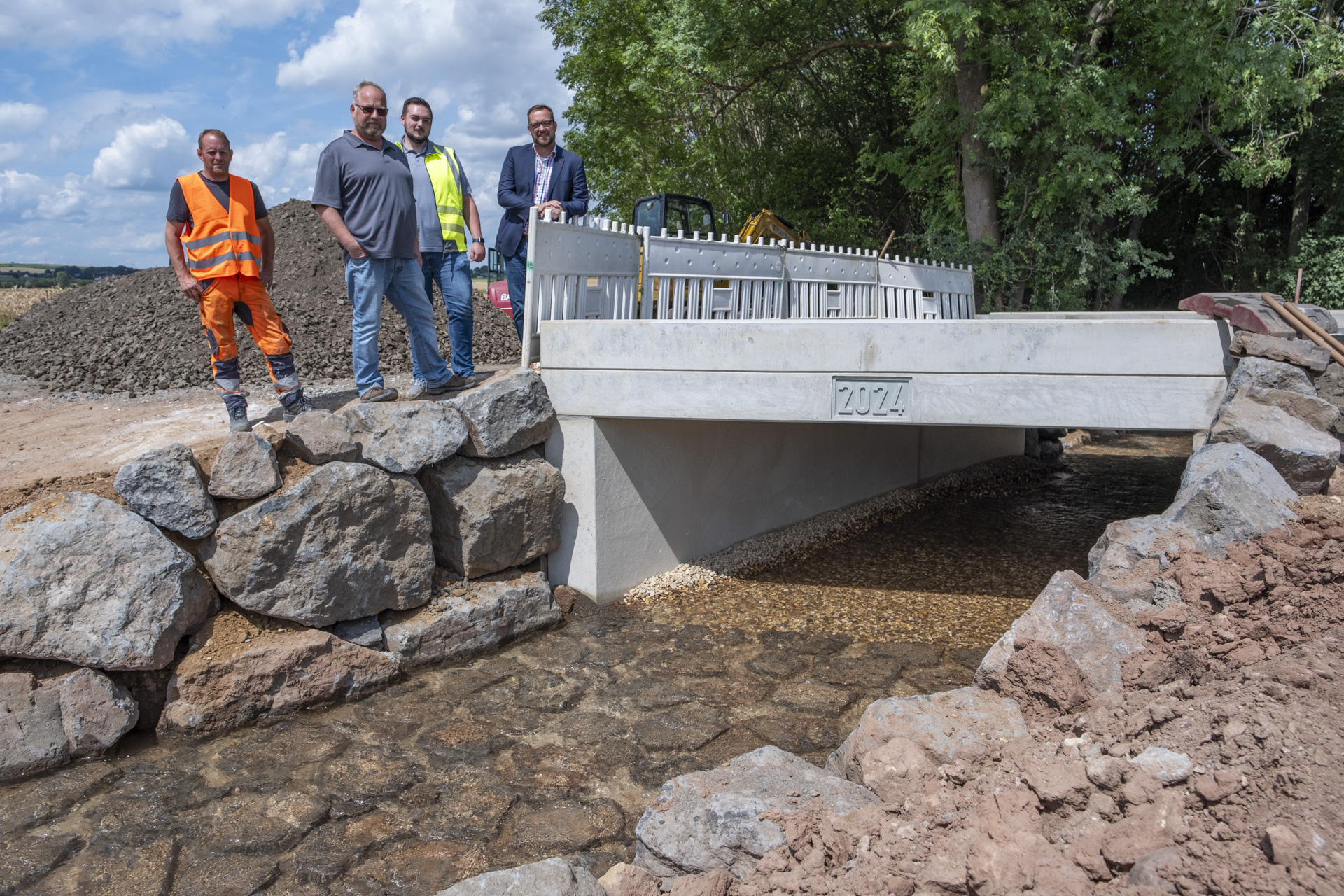 4 Männer stehen an der noch noch durch einen Baustellenzaun gesperrten neuen Brücke in Floisdorf.